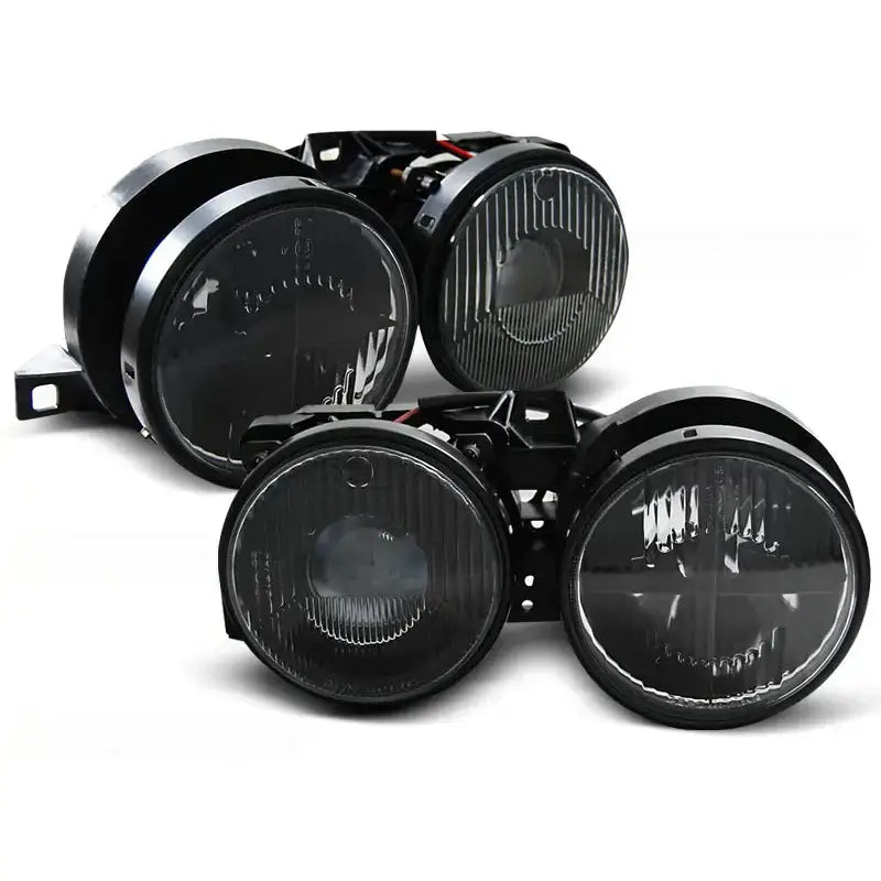 Frontlykter Bmw E30 med sort innfatning og ribbet glass, fire runde lykter sett fra vinkel.