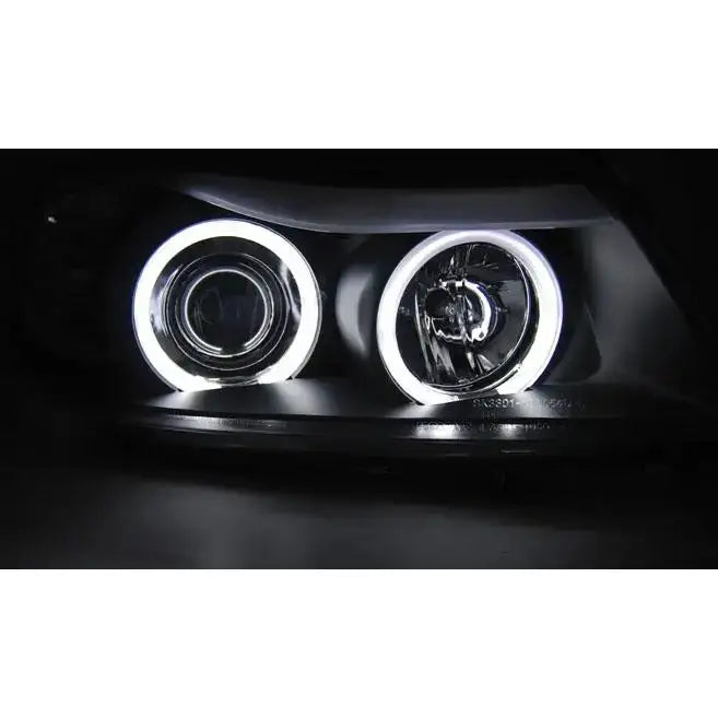 Hovedlys Bmw E90/E91 Angel Eyes CCFL Black med hvite LED-ringer og kromdetaljer i mørkt miljø.