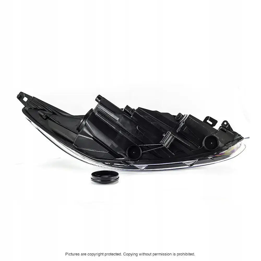 Hovedlykter Ford Fiesta 13-17 i sort plast, sett fra siden med monteringspunkter og løs rund del foran.