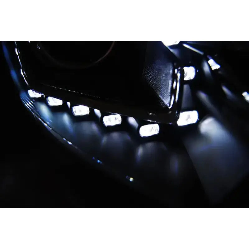 Hovedlys Ford Focus Mk3 med buet rekke hvite LED-lys på blank sort overflate i mørkt miljø.