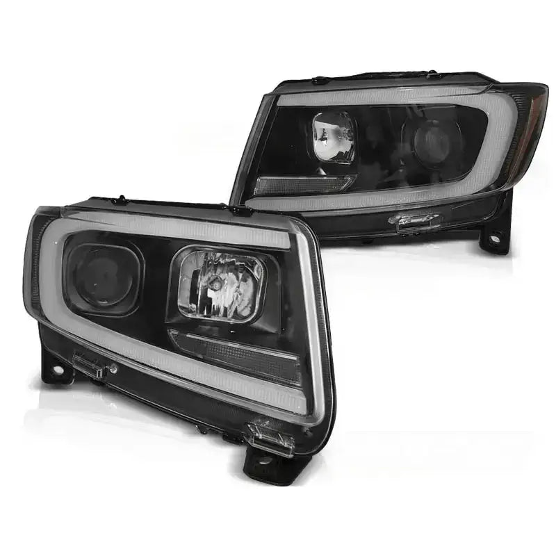 Frontlykter Jeep Grand Cherokee 11-13 med sort ramme, LED-lysstripe og klare linser, sett fra skrå vinkel.