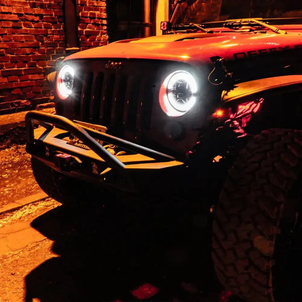 Headlamp LED Ring Truck Lite montert på Jeep Wrangler JK med robuste runde frontlykter i mørket.