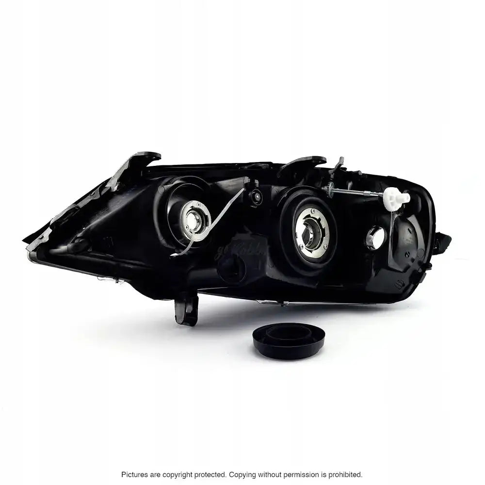 Headlamp bakside av Opel Astra G frontlykt med runde metallfester og justeringsskrue på hvit bakgrunn.