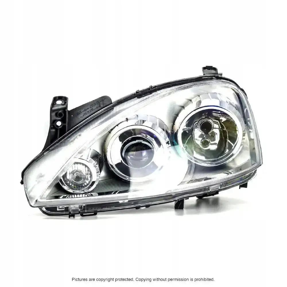 Hovedlys Opel Corsa C frontlykt med klar plastlinse og kromdetaljer, sett forfra mot hvit bakgrunn.