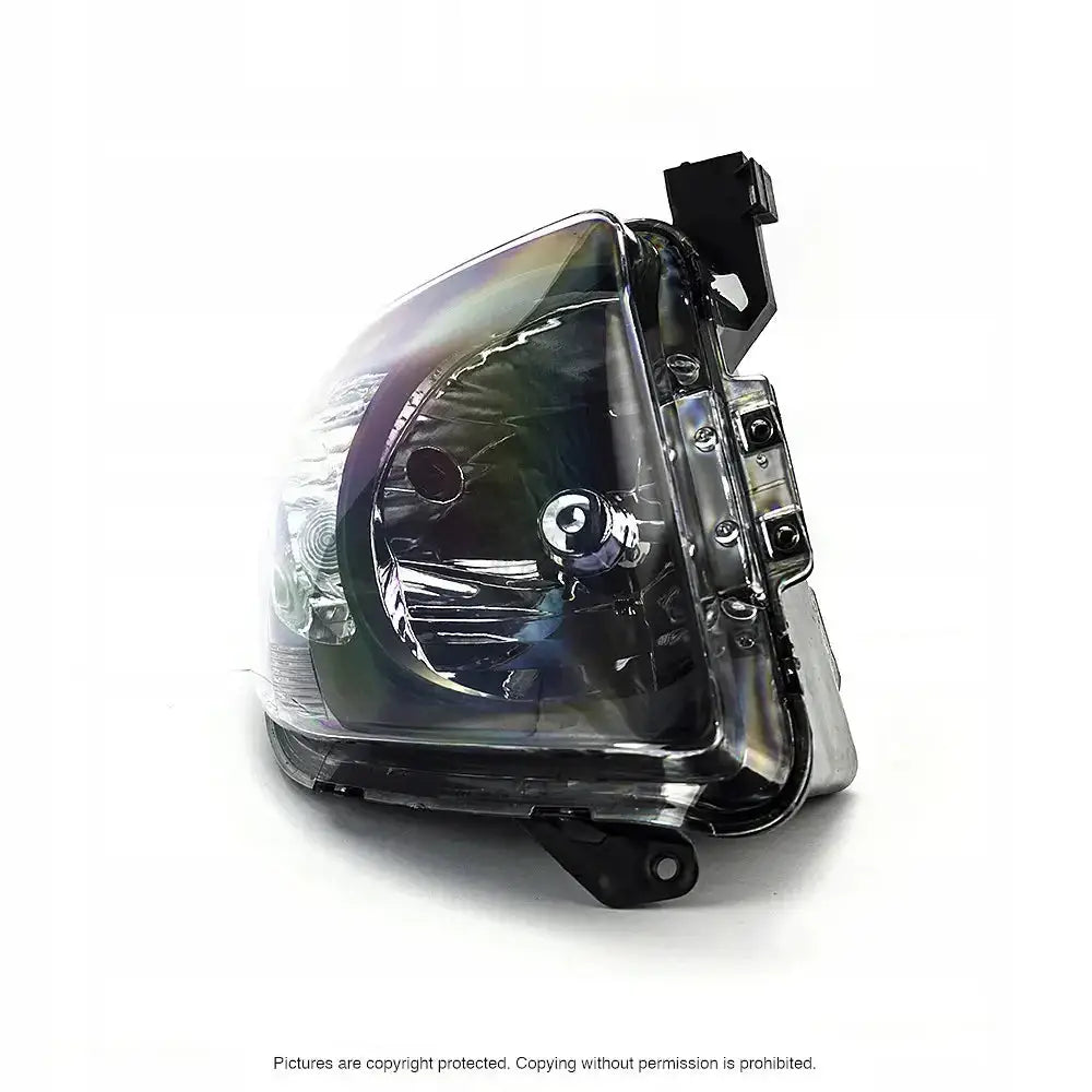 Hovedlys Suzuki Swift 05-07 H4 i klart plast og krom, sett fra skrå vinkel med synlige festebraketter.