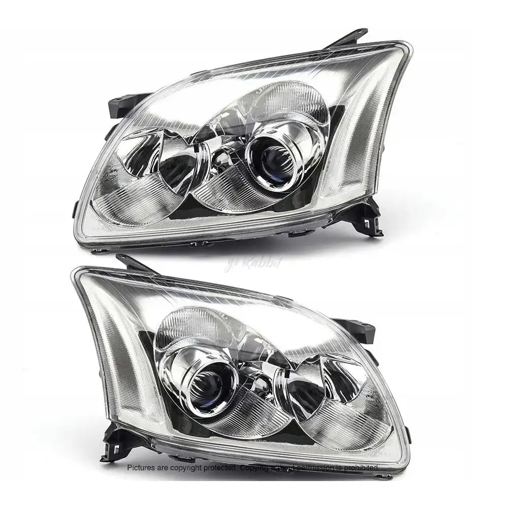 Frontlykter Toyota Avensis T25 03-06 halogen, to klare lykter med kromdetaljer sett fra skrå forside.