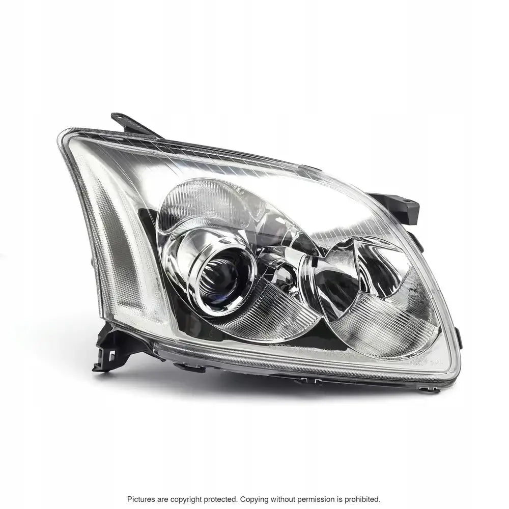 Headlamp for Toyota Avensis T25 03-06 halogen, skrå forside med klart glass og kromdetaljer.