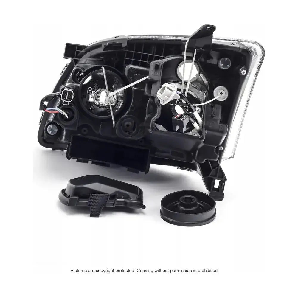 Hovedlys Toyota Avensis T25 halogen sett bakfra med synlige pærer og løse deksler på hvit bakgrunn.