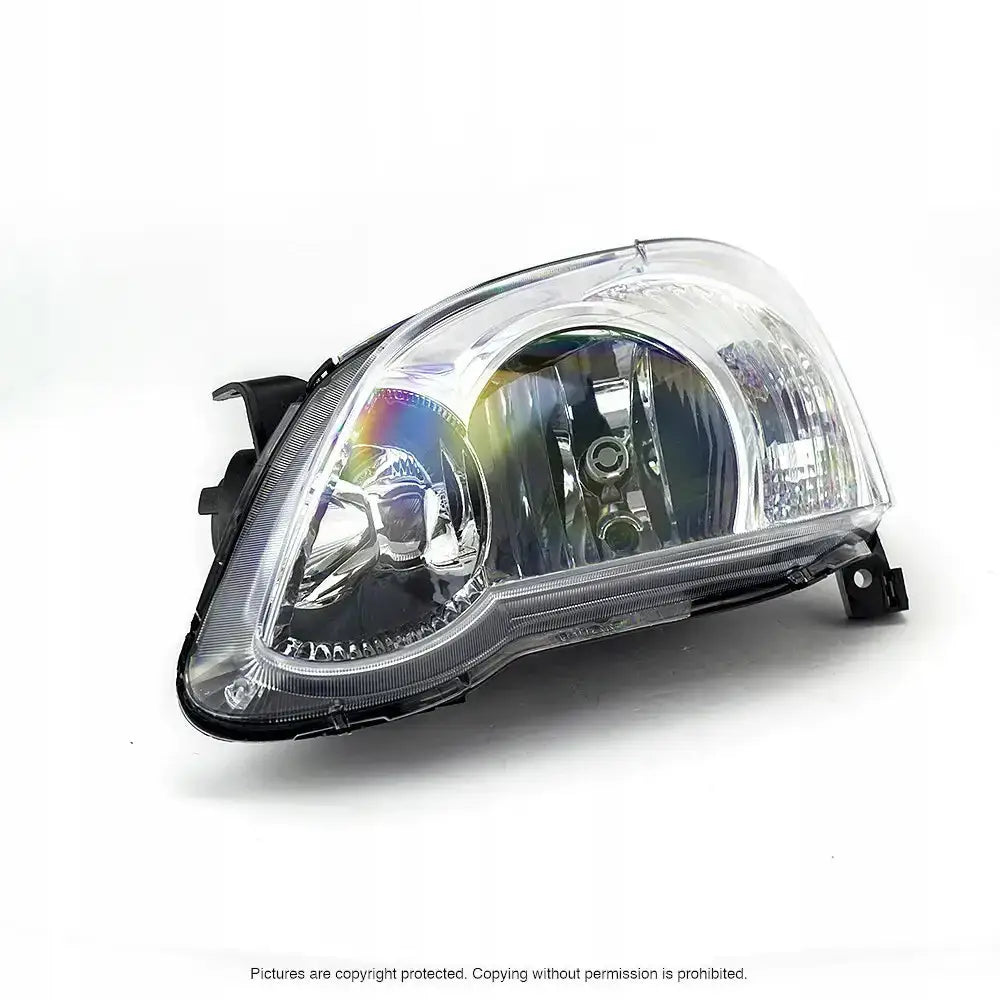 Hovedlykter Toyota Corolla E12 04-07 H7 i klar plast og krom, sett fra skrå forside mot hvit bakgrunn.