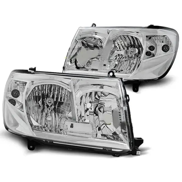 Frontlykter Toyota Land Cruiser J100 05-07 i klar plast og krom, vist fra skrå vinkel med sorte fester.