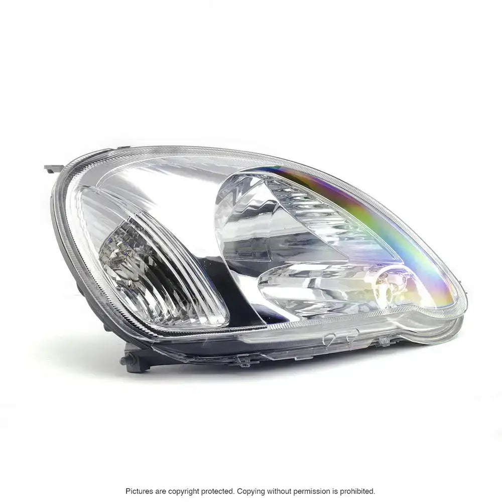 Hovedlykter Toyota Yaris 03-05 H4 i klar plast med kromdetaljer sett fra skrå frontvinkel.