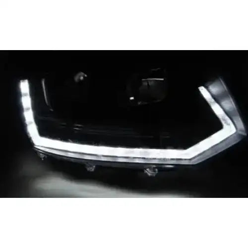Hovedlykter Vw T5 Tube Light T6 Look Black med LED lyststripe, sett fra skrå front i mørkt miljø.