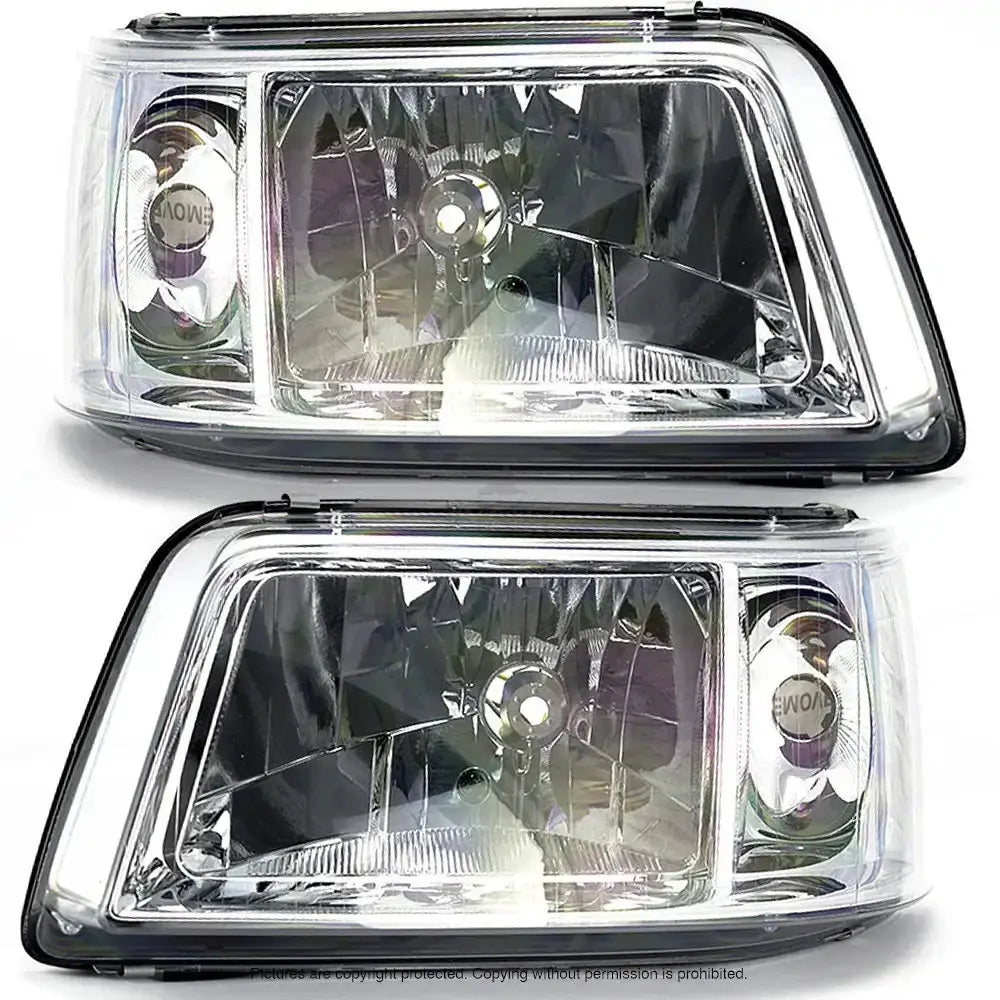 Frontlykter i klart glass med sølvfargede refleksoverflater, sett skrått forfra mot hvit bakgrunn.