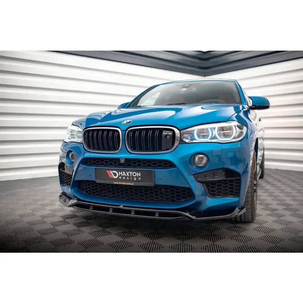 Front splitter på blå BMW X5 M F15 med sorte luftinntak og LED-lykter, sett forfra innendørs.