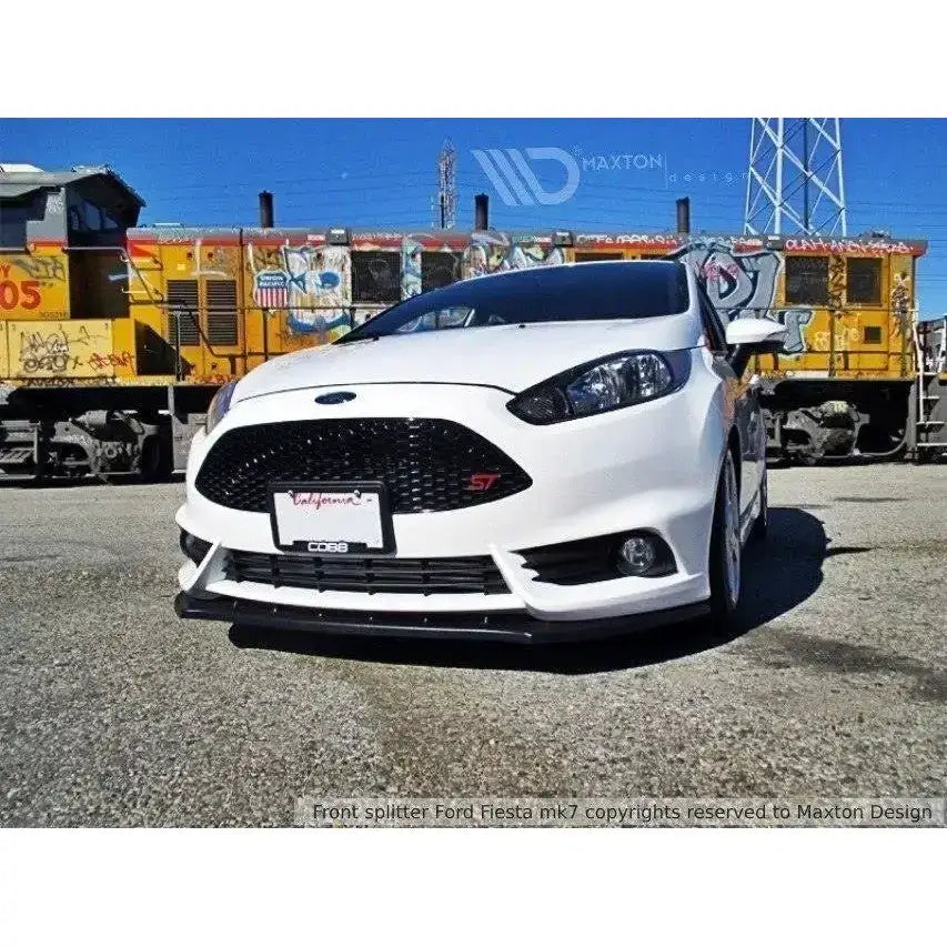Front splitter på hvit Ford Fiesta Mk7 St Facelift 2013-2016 med sort grill, tog i bakgrunnen.
