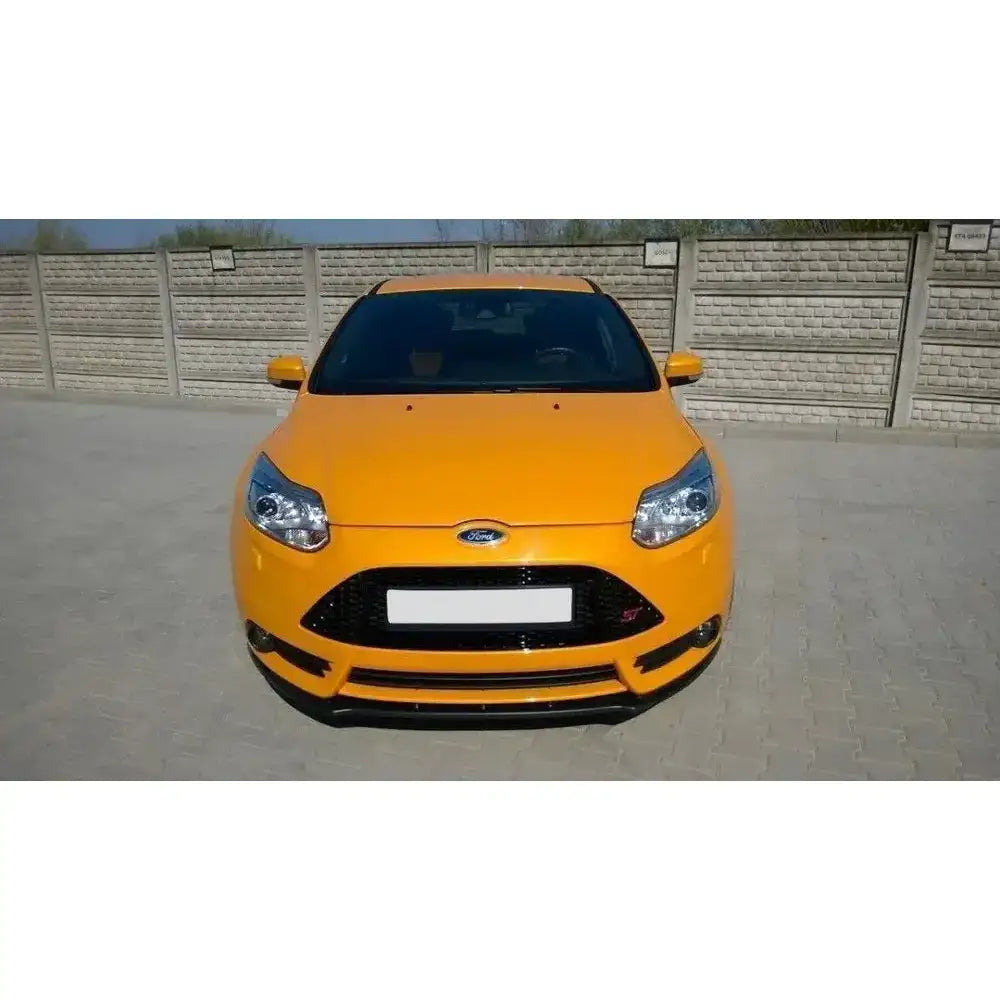 Frontleppe på gul Ford Focus Mk3 St Preface med sort grill, sett forfra parkert foran murvegg.