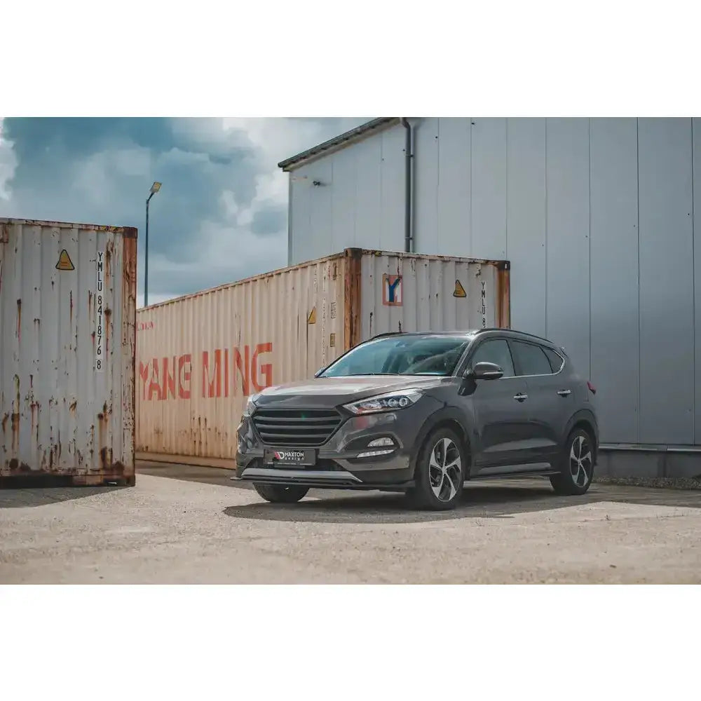 Frontleppe på Hyundai Tucson Mk3 SUV parkert foran hvite containere og industribygg.