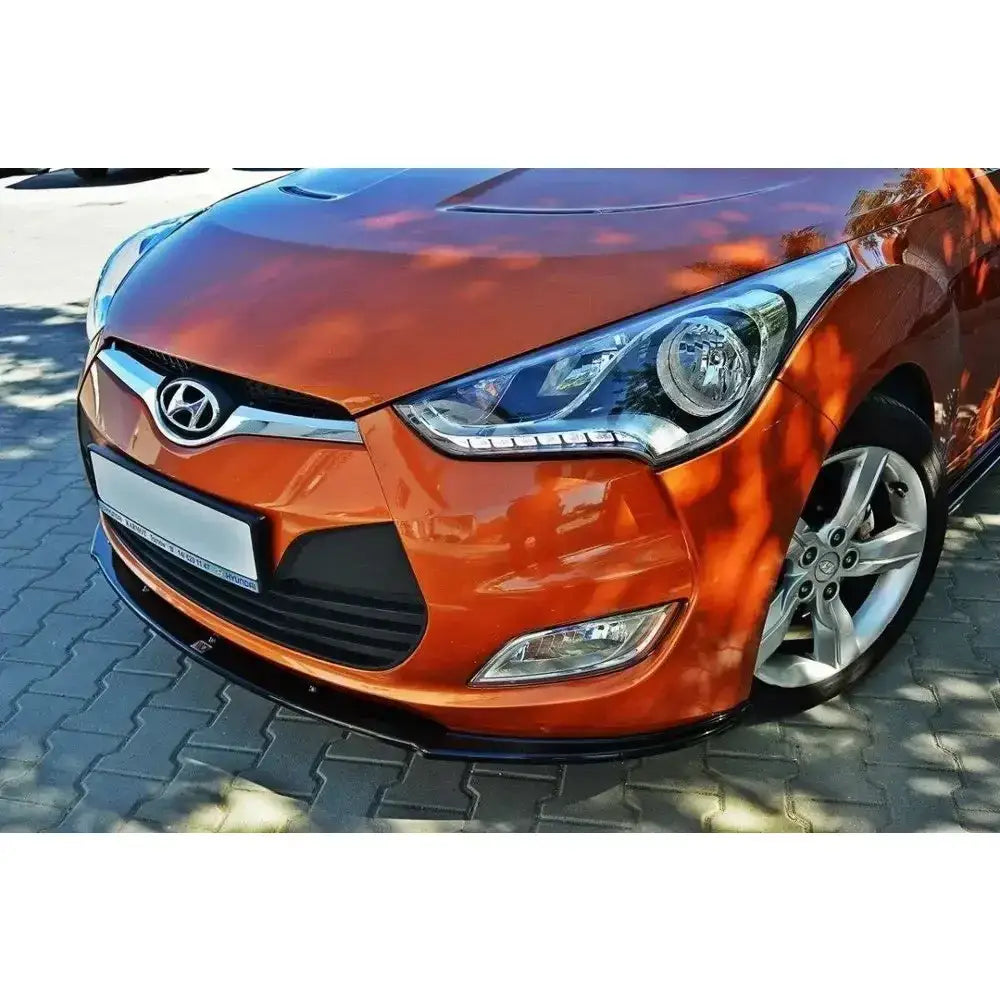 Spoiler på Hyundai Veloster, oransje bil med markant frontfanger og sølvfelger på steinbelagt underlag.
