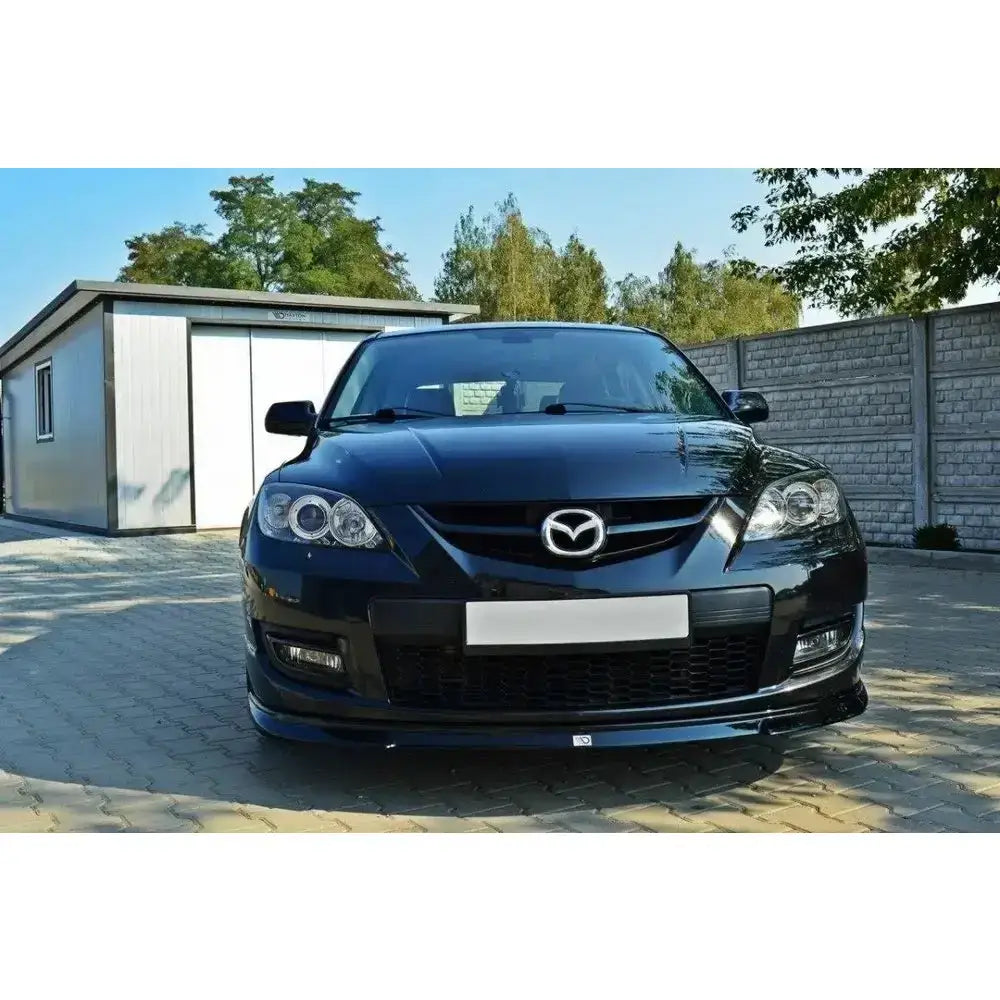 Front lip på Mazda 3 MPS Mk1, svart bil sett forfra med logo, parkert foran murvegg og bygg.