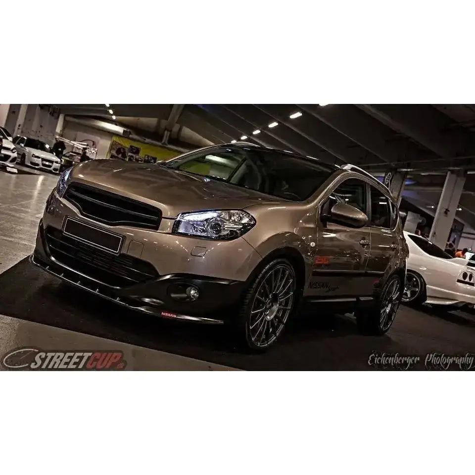 Frontleppe på Nissan Qashqai facelift, sølv SUV med mørke felger og sorte detaljer på bilutstilling.