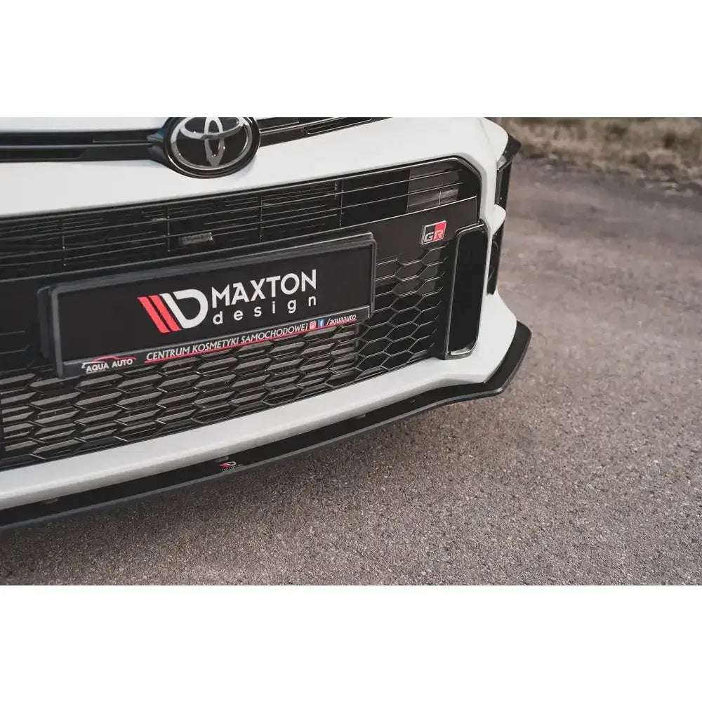 Front splitter til Toyota GR Yaris MK4 med karbon-look og Maxton Design-logoer, nærbilde parkert på asfalt.