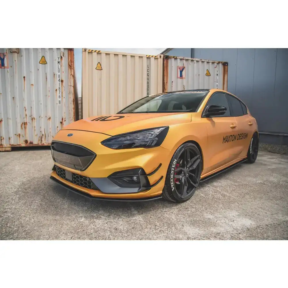 Front splitter på Ford Focus ST med svarte detaljer, sportsfelger og logo foran rustne containere.