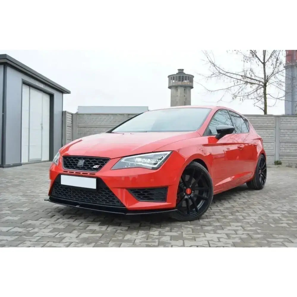 Frontspoiler på rød Seat Leon III Cupra med sorte felger, skarpe lykter og lav kjørehøyde på brostein.