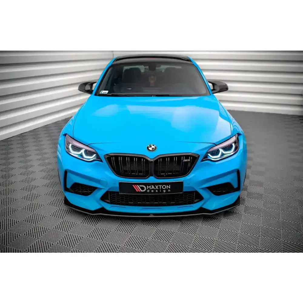 Spoiler på BMW M2 Competition F87 med svarte detaljer og LED-frontlykter, sett forfra mot lys vegg.
