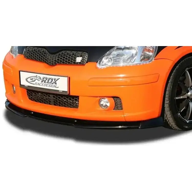 Frontspoiler Toyota Yaris TS 03-05 i svart plast montert på oransje bil, sett forfra fra skrå vinkel.