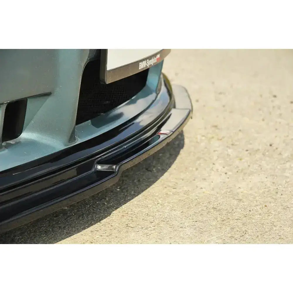 Front lip på BMW M3 E36 V.1, sort blank plast, nærbilde fra skrå vinkel mot asfalt.