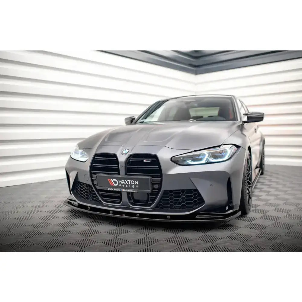 Front lip på BMW M4 G82 V.1 21- med sorte detaljer, sett forfra på rutet gulv innendørs.