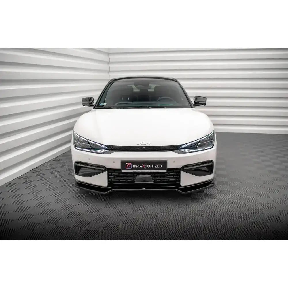 Frontleppe på hvit Kia EV6 GT-Line Mk1 med sorte detaljer og LED-lykter, sett rett forfra innendørs.