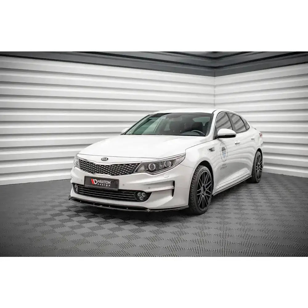 Frontleppe på hvit Kia Optima Mk4 V.1 med sorte felger, vist skrått forfra i lyst rom med rutete gulv.