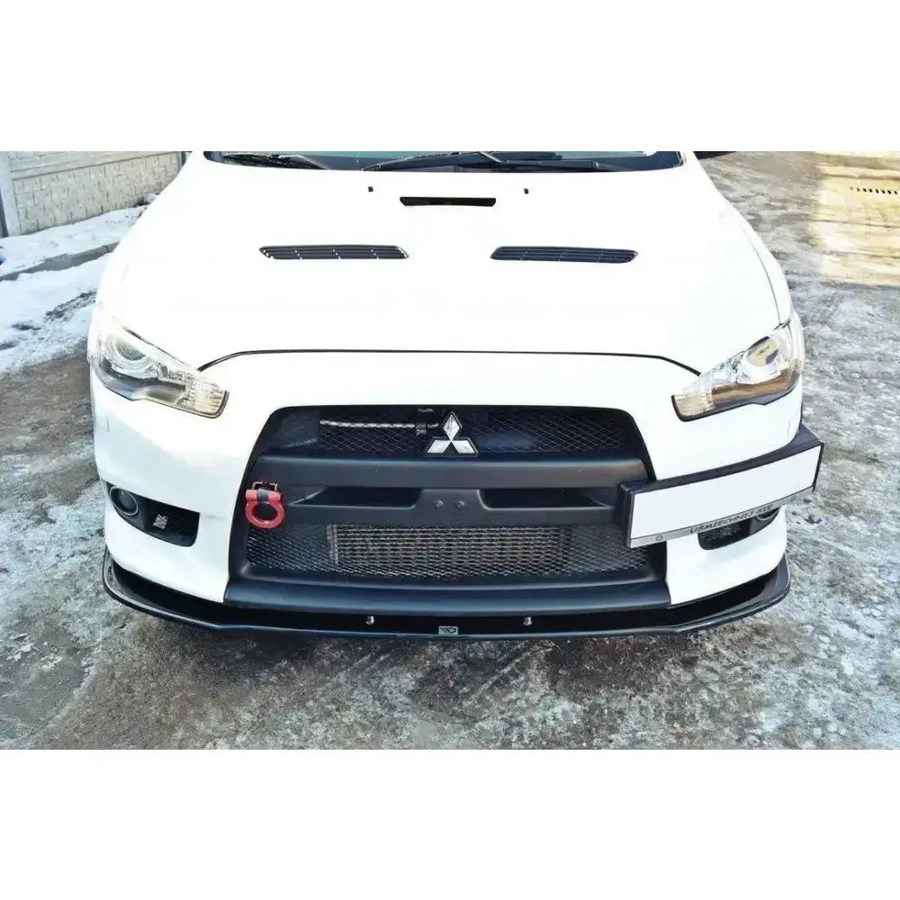 Front splitter på Mitsubishi Lancer Evo X V.1 med sort grill, rød slepekrok og snødekt bakgrunn.