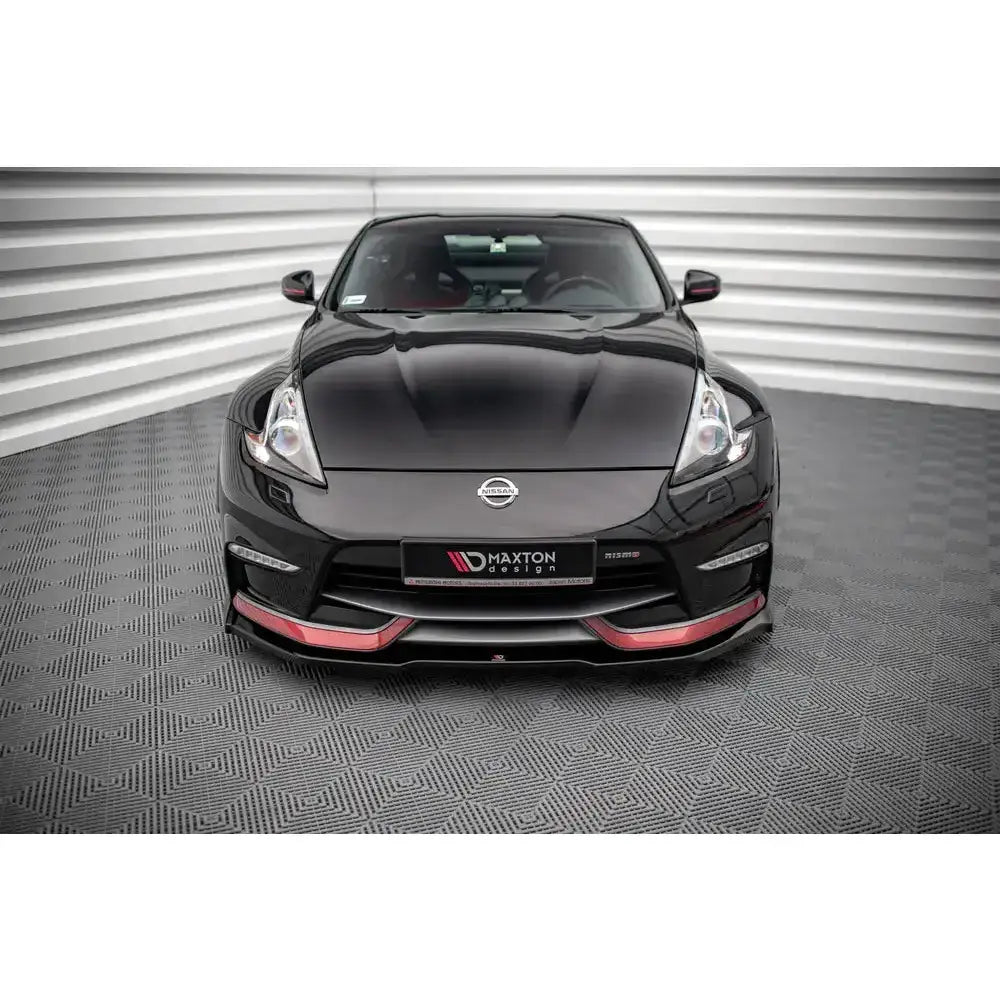 Frontleppe på sort Nissan 370Z Nismo Facelift med røde detaljer, sett forfra på grått gulv.