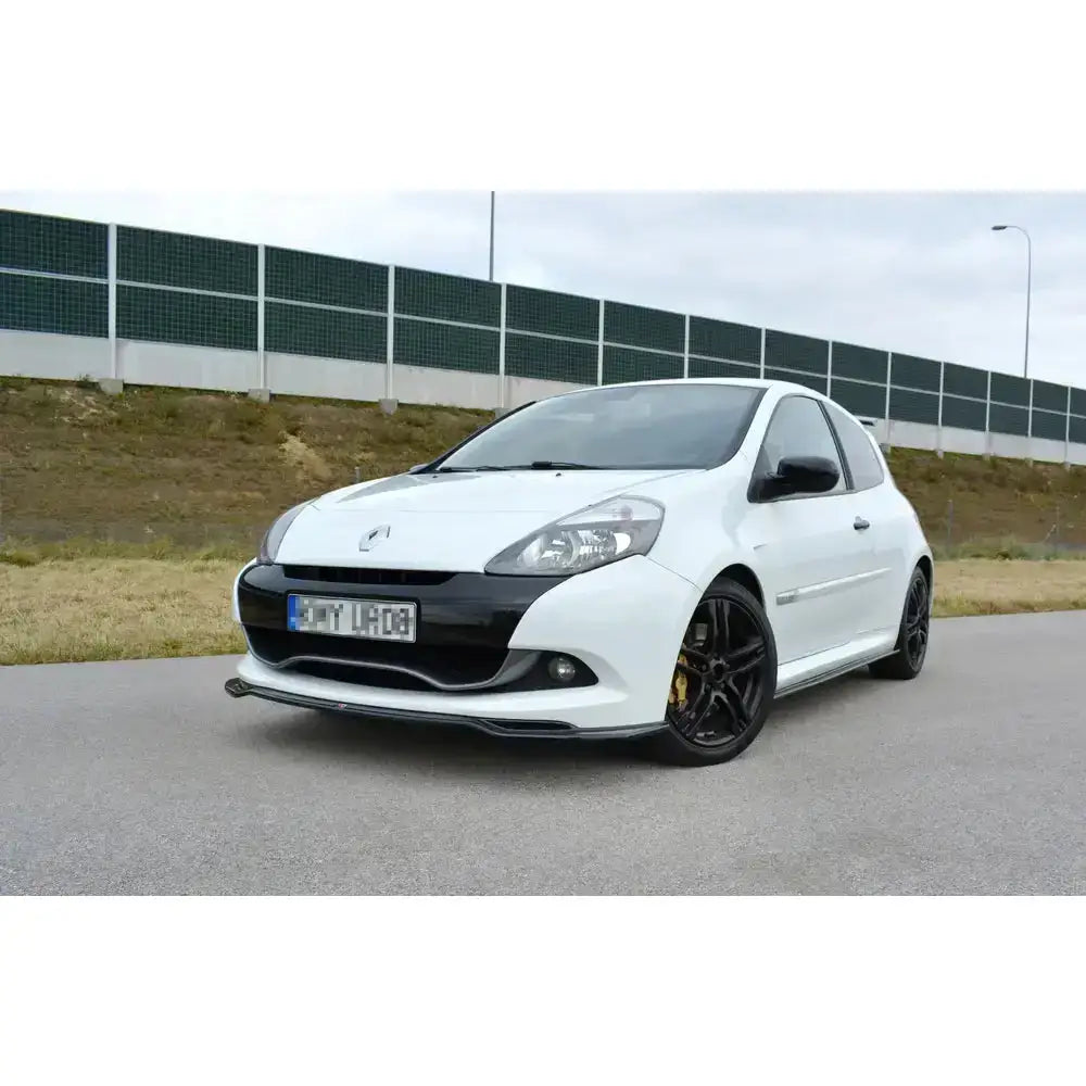 Frontspoiler på Renault Clio Mk3 Rs Facelift, hvit bil med sorte felger, parkert foran støyskjerm.