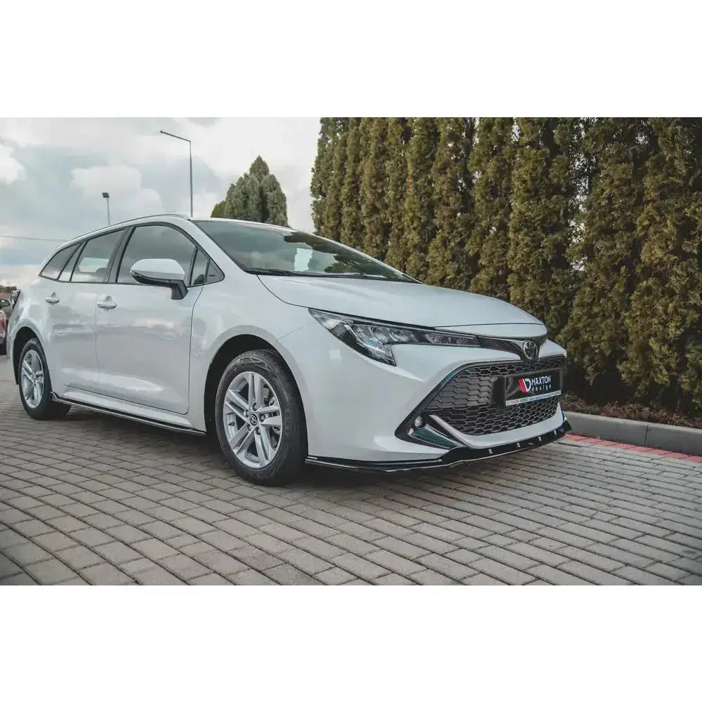 Frontspoiler på hvit Toyota Corolla XII Touring Sports med aluminiumsfelger, parkert på steinlagt underlag.