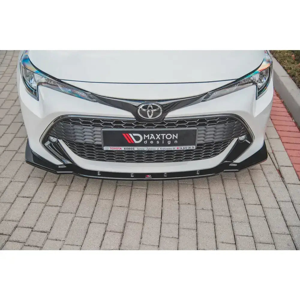 Spoiler til Toyota Corolla XII, nærbilde av sort frontspoiler under grill på hvit bil, sett ovenfra.