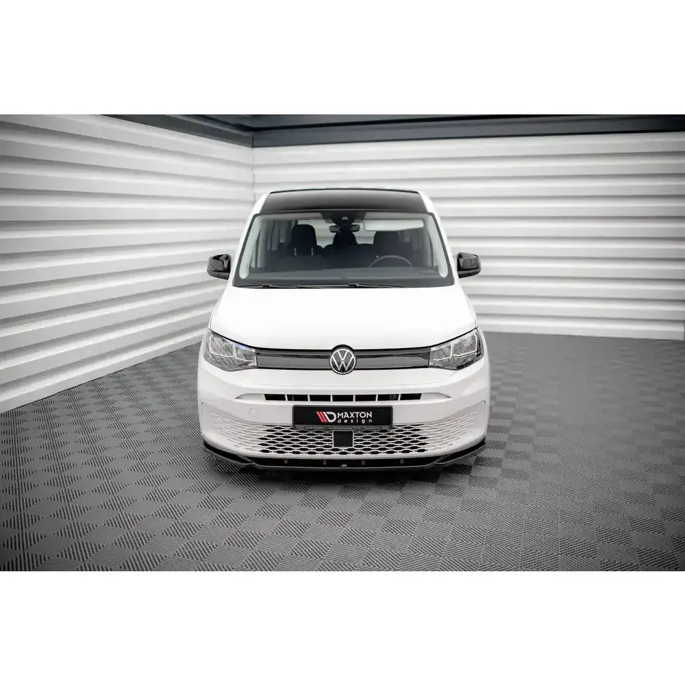Spoiler til Volkswagen Caddy Mk5 V.1 montert foran på hvit bil med mørke detaljer, sett forfra.