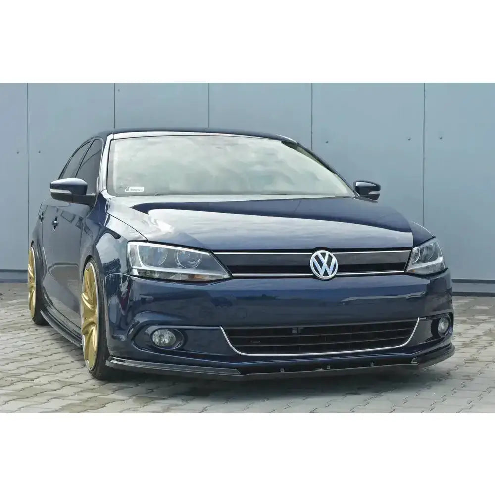Front splitter på Volkswagen Jetta Mk6 sedan i mørkeblått med gullfelger, sett forfra på steinlagt bakke.