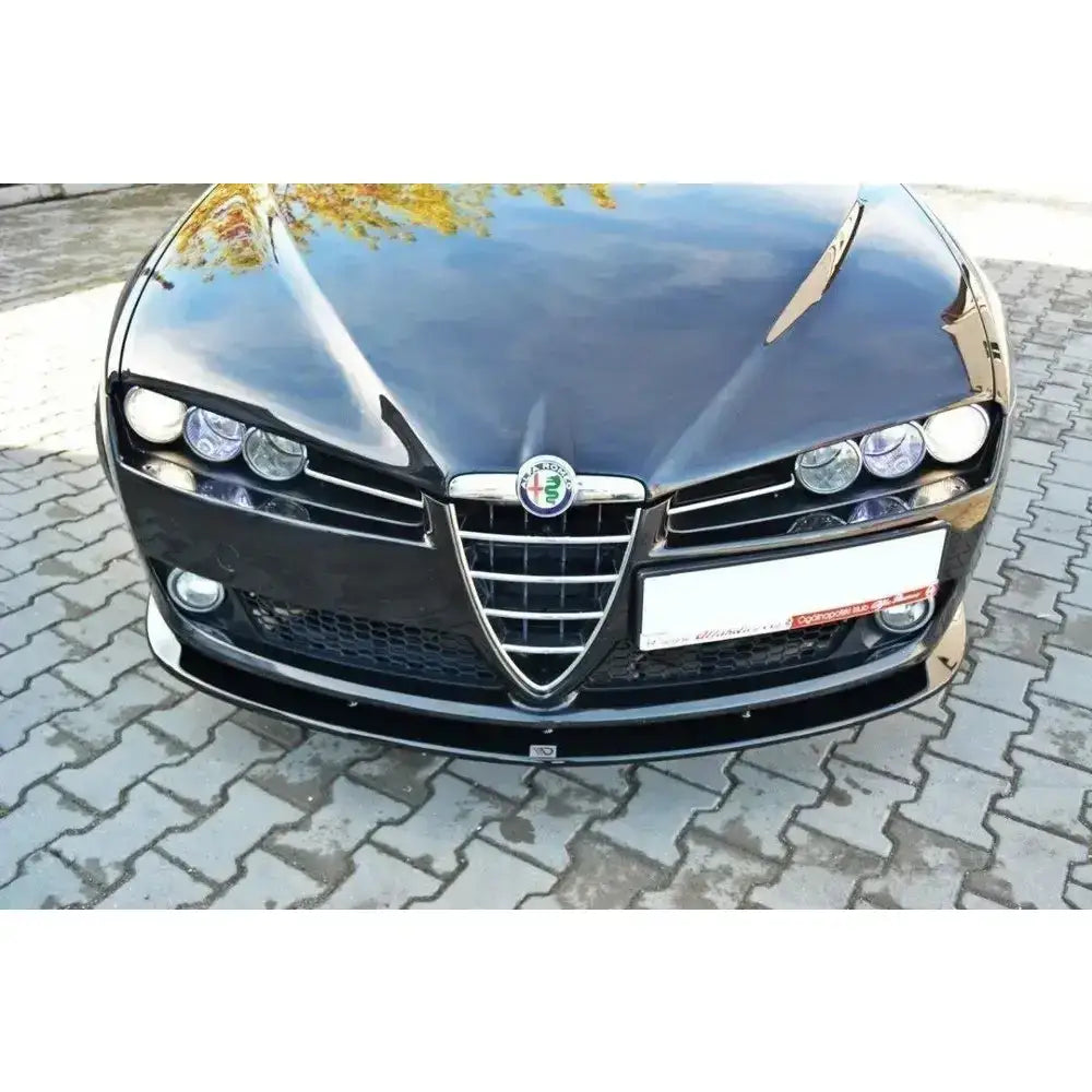 Frontleppe på Alfa Romeo 159 V.2, sort bilfront med kromgrill og markerte frontlys mot steinlagt bakgrunn.