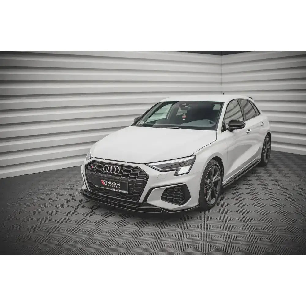 Front lip på hvit Audi S3 med svart grill, parkeringssensorer og sportsfelger i fotostudio.
