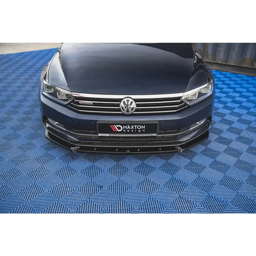 Spoiler Volkswagen Passat B8 V.2 sett forfra med sort, blank frontsplitter mot blått mønstret underlag.