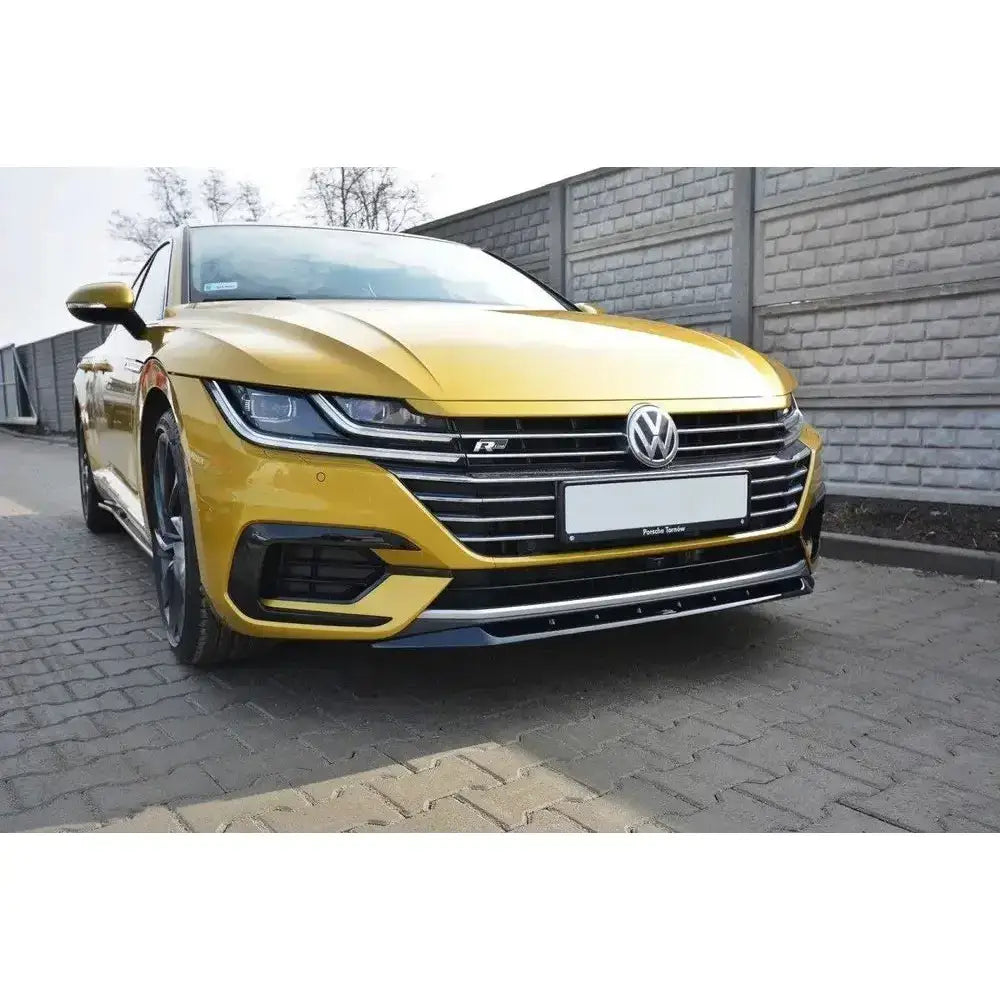 Spoiler på VW Arteon V.2 i gul metallic sett skrått forfra med svarte og krom detaljer ved murvegg.