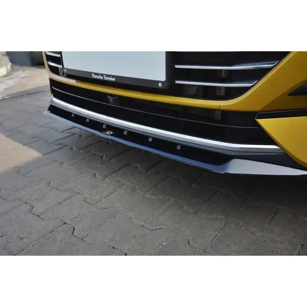 Front splitter på VW Arteon V.2, nærbilde av svart og sølv spoiler på gul bil over brostein.