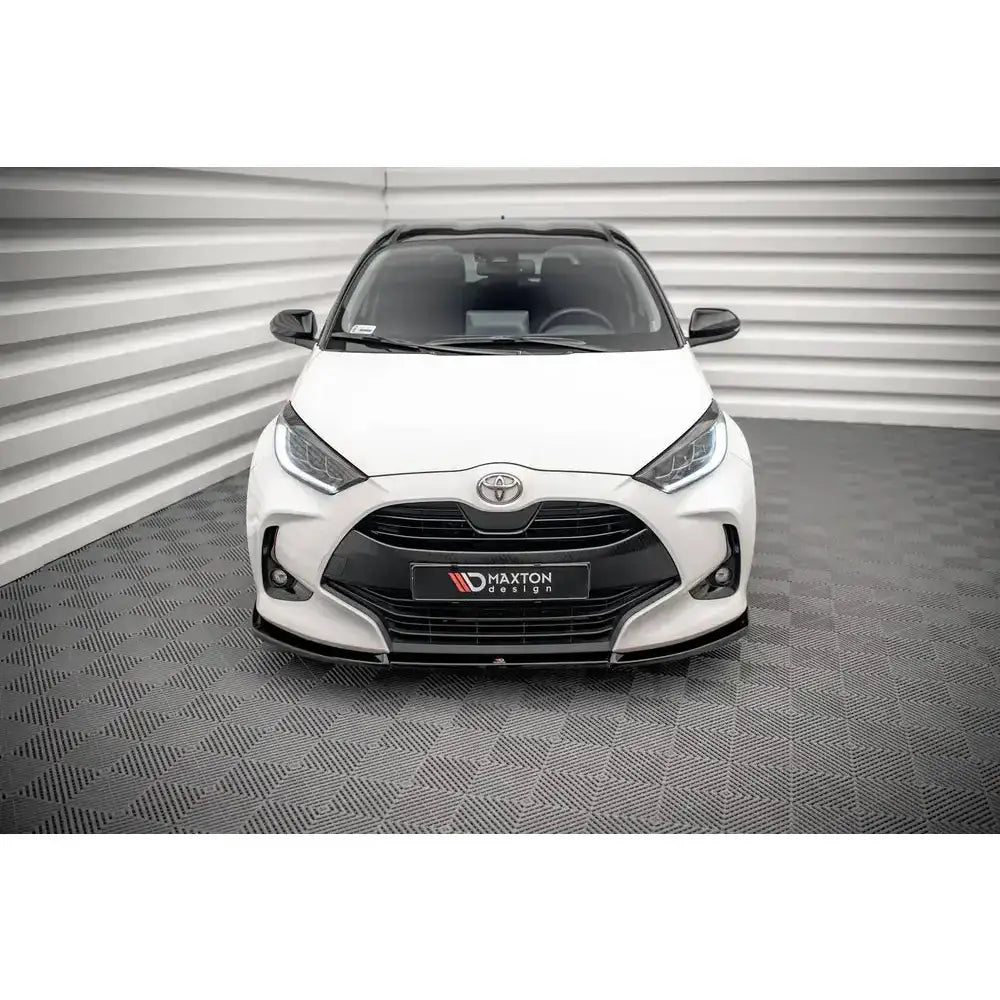 Frontleppe på hvit Toyota Yaris Mk4 V.3, sett forfra med sort grill og stilrene frontlykter.