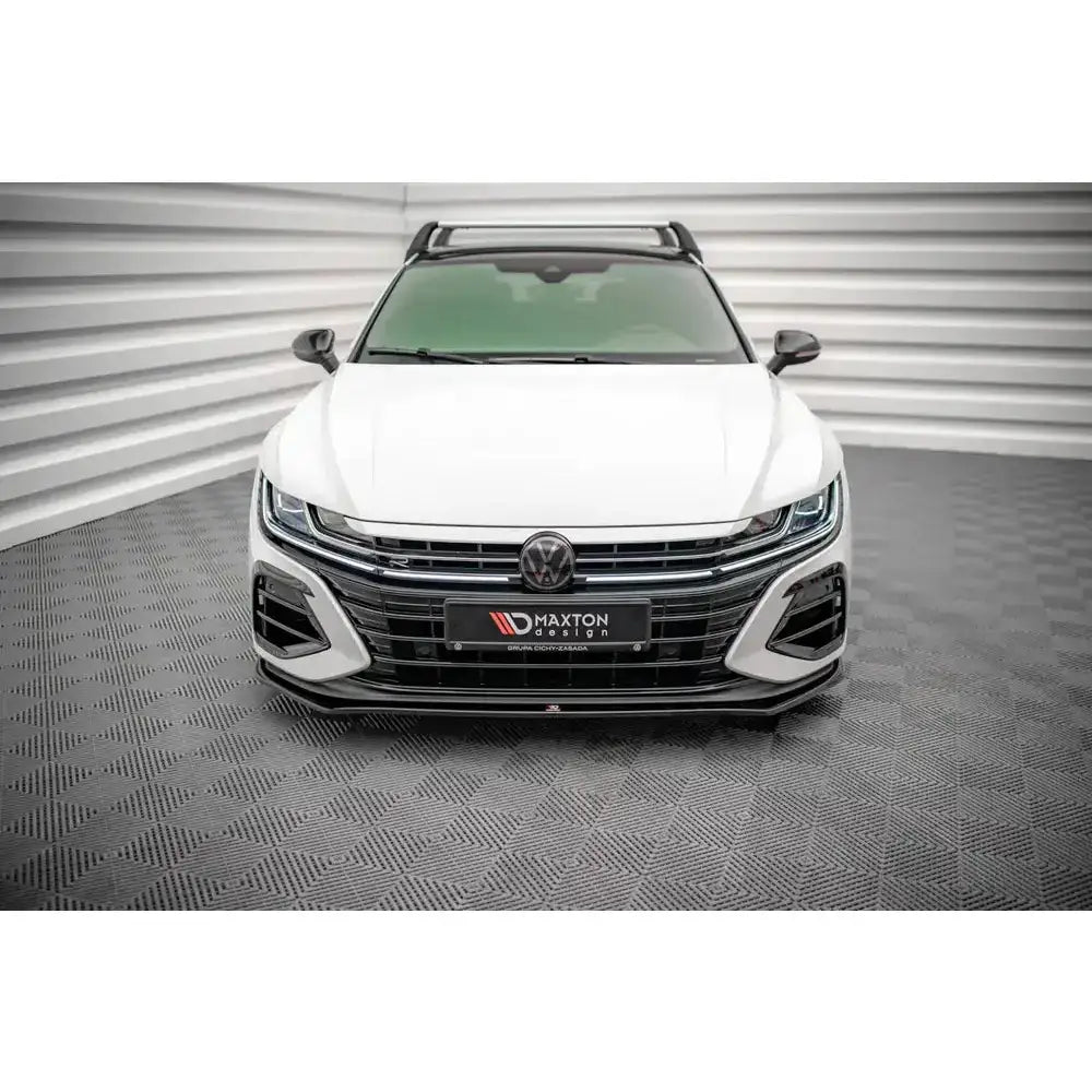Frontleppe på hvit Volkswagen Arteon R med mørke takrails og blank grill, sett forfra innendørs.