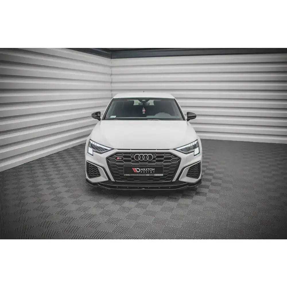Frontsplitter på hvit Audi S3 med sort grill og LED-lykter, fotografert rett forfra i lyst rom.