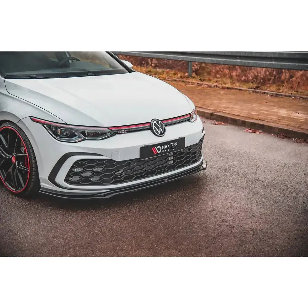 Spoiler på Volkswagen Golf 8 GTI V.4 med sort grill og rød stripe, nærbilde på våt asfalt.