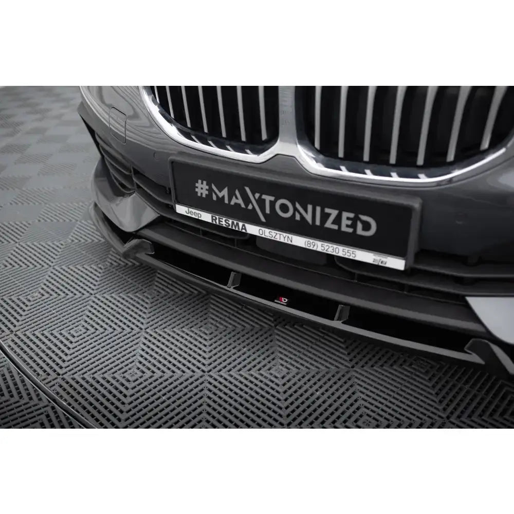 Front lip på BMW 1 F40 V.1, nærbilde av sort spoiler mot grå bil og kromgriller, sett ovenfra.